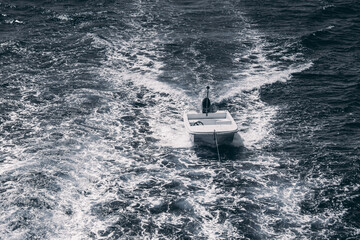 Fototapeta premium View of an empty motorboat tied behind the main yacht surrounded by ocean waves and a strong water wake from the primary vessel