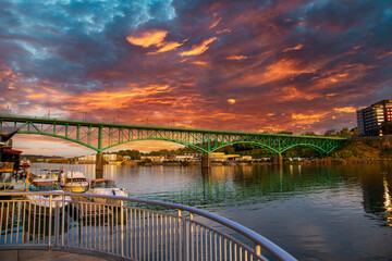 a gorgeous autumn landscape along the Tennessee River with boats docked and the Gay Street Bridge over the water with powerful red clouds at sunset in Knoxville Tennessee USA - obrazy, fototapety, plakaty