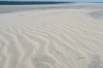 Dry sand has ripple waves from blowing wind over the land surface, though close to the shore, the...