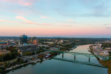 aerial shot of the Gay Street Bridge over the Tennessee River surrounded by autumn colored trees, lush green trees and office buildings with powerful clouds at sunset - obrazy, fototapety, plakaty