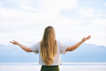 Young blond woman with arms wide open enjoy landscape of cloudy mountains, back view