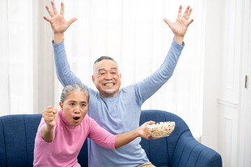 Fototapeta na wymiar Excited mature couple, Senior man and woman watching tv, senior sport fans celebrating favorite team victory, sitting on cozy couch and eating popcorn snack at home, enjoying weekend. Happy senior.