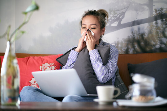 mature asian woman catching a cold working from home using laptop computer