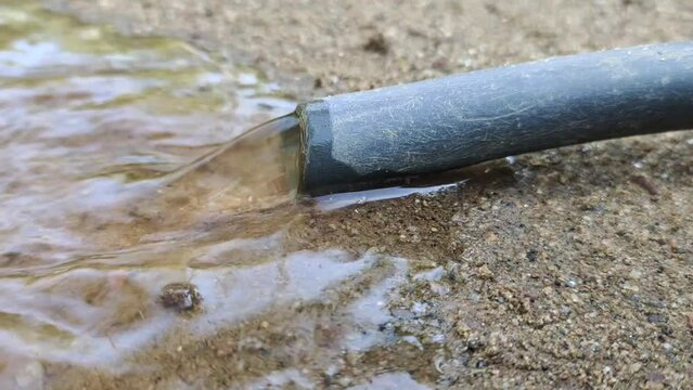 Wasting or wastage of natural resource clean water by flowing or gushing out from garden irrigation hose pipe tube isolated on ground soil. Save and conserve fresh water concept. Close up macro view.