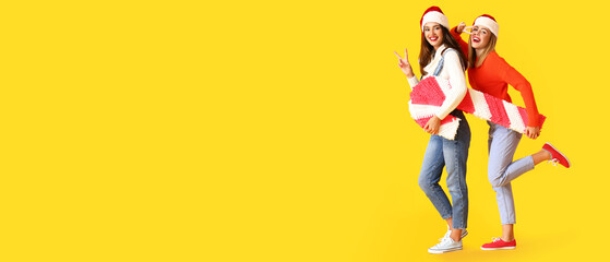 Fototapeta na wymiar Young women in Santa hats and with candy cane pinata on yellow background with space for text