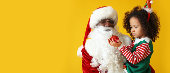 Little African-American girl and Santa Claus on yellow background with space for text