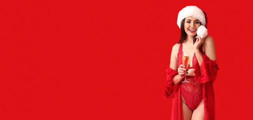 Sexy young woman in Santa hat and underwear drinking champagne on red background with space for text