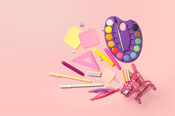 Shopping cart, watercolor paints and stationery supplies on color background