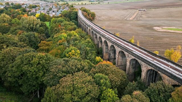 Drone footage of the Penistone Railway Station and stone built viaduct near Barnsley, South Yorkshire. Showing a ploughed field, bridge, woodland and railway tracks.