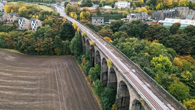 Drone overhead footage of the Penistone Railway Station and Viaduct near Barnsley, South Yorkshire. Showing a ploughed field, bridge, woodland and railway tracks.