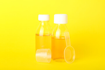 Bottles of cough syrup, spoon and cup on yellow background