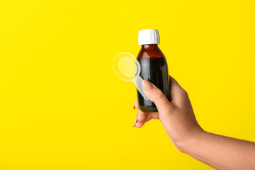 Woman with bottle of cough syrup and spoon on yellow background