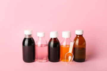 Bottles of cough syrup and spoon on pink background