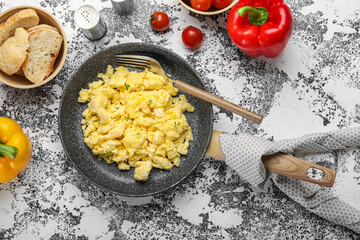 Frying pan of tasty scrambled eggs, vegetables and bread on grunge background