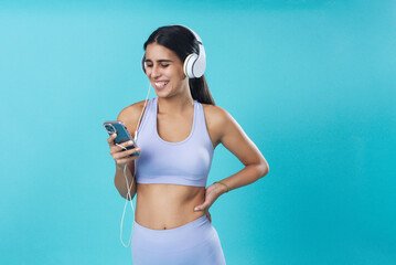 Young beautiful girl preparing playlist and listening to music for her workout, pastel colored gym training session; teal studio background