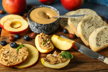 Wooden board of tasty apple rounds and wedges with nut butter, closeup