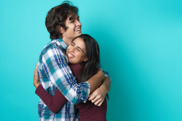 Happy couple in love hugging, embracing each other; casual wear, teenage years, fresh relationship; teal studio background