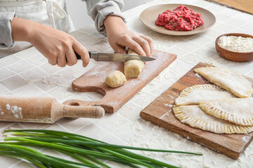 Woman cutting dough for chebureks at table, closeup