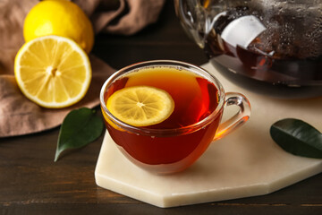 Board with glass cup of black tea and lemon on dark wooden background, closeup