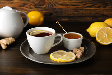 Plate with cup of black tea, lemon, cane sugar and honey on dark wooden background