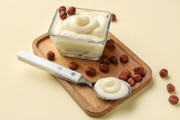 Wooden board with tasty vanilla pudding and hazelnuts on color background