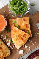 Wooden board with tasty chebureks and green onion on table, closeup