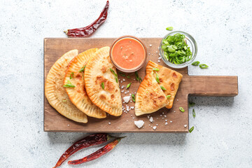 Wooden board with tasty chebureks, sauce, green onion and chili peppers on light background