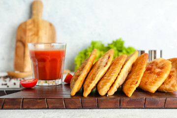 Wooden board with tasty chebureks and glass of tomato juice on light table, closeup
