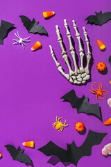 Obraz na płótnie Canvas Frame made of Halloween treats, paper bats and skeleton hand on purple background