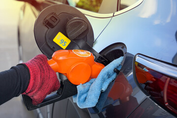 Gasoline filling nozzle 95 orange in the hand of the employee to fill the black car with gas. Soft...