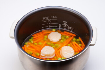 調理中の写真　ホタテとニンジンの炊き込みご飯　炊飯器の内釜にお米と人参、ホタテの貝柱、酒、醤油、グリンピースを加えて炊く　日本