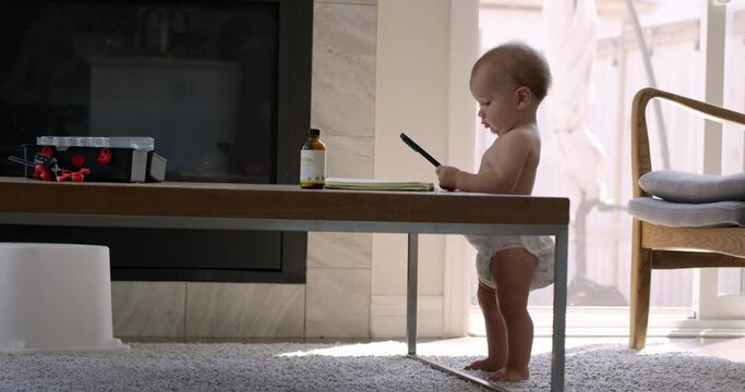 Baby girl 1 year old plays with smart phone while standing up on coffee table - copying parents behavior