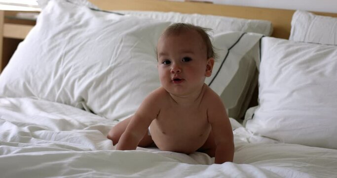 Baby firl 1 year old lays on bed and shakes head towards camera - adorable baby