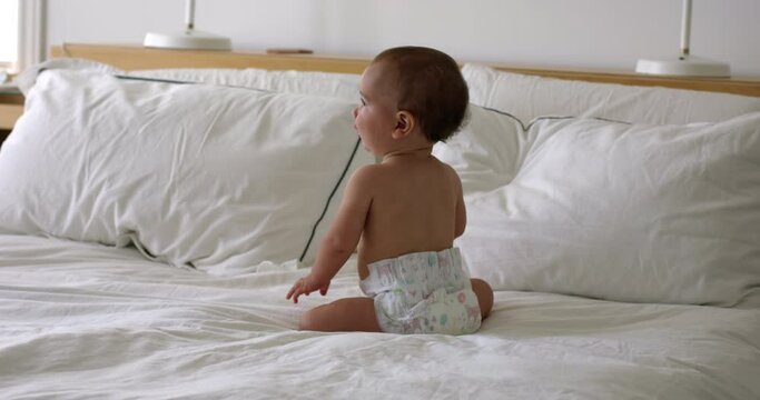 Baby girl sits and bounces on bed happy and excited - wide shot