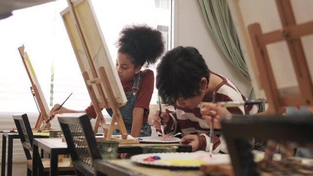 Group of multiracial little children concentrates on acrylic color picture painting on canvas in an art classroom and creatively learns with talents and skill at the elementary school studio education