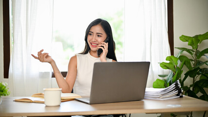 Gorgeous Asian female account executive is talking on the phone with her business partner
