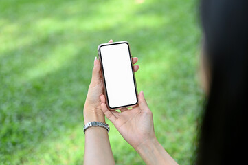 A young Asian female holding a mobile phone mockup over blurred grass background
