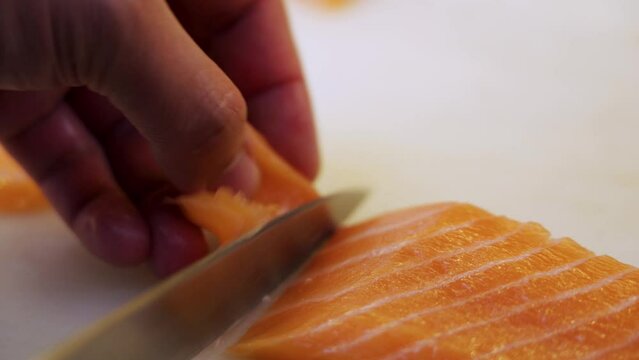 Cleseup of cutting sashimi and nigiri pieces from salmon flank by sushi master chef.