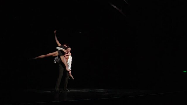 Latin-American ballroom dancers couple.Man brings woman on dark stage,picks her up,rotates her turning around his neck,puts her bented on shoulder,spinning around holding her leg in beautiful pose.