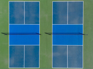 Two blue and green tennis courts with sand taken from a sky view aerial drone