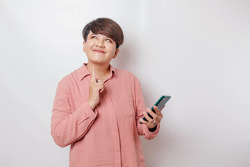 Fototapeta premium A portrait of a happy Asian woman is smiling and holding her smartphone wearing a pink shirt isolated by a white background