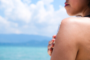 A woman is applying sunscreen and skin care to protect her skin from UV rays. She was putting sunscreen on her shoulders. sunny background Health and skin care concept