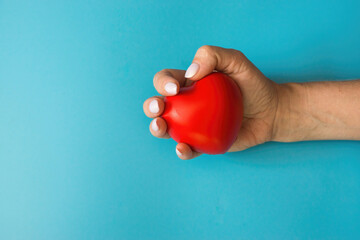 female hand holds a red heart on a blue background on the left copyspace.health of the woman's...