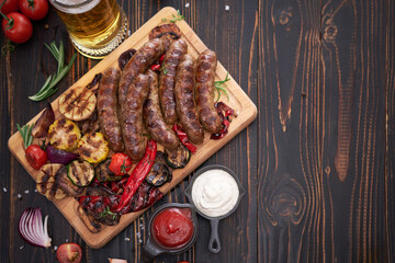 Grilled sausages and vegetables on wooden cutting board at domestic kitchen