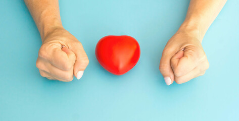 Obraz premium woman's hands clenched in fists and red heart blue background. Hard anger and hatred concept. Treason and betrayal in the family. single woman. love plot. love triangle