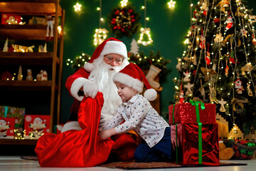 Fototapeta na wymiar Little boy in Santa's hat takes out gifts from Santa claus sack. Christmas time. New Year concept