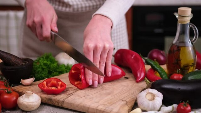 Woman cutting slicing fresh red pepper with a knife on a wooden board