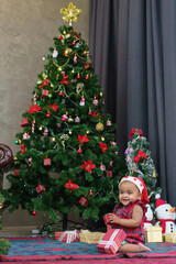 Happy African American baby girl in Santa Claus costume smiling and sitting with present boxes at the Christmas tree on holidays
