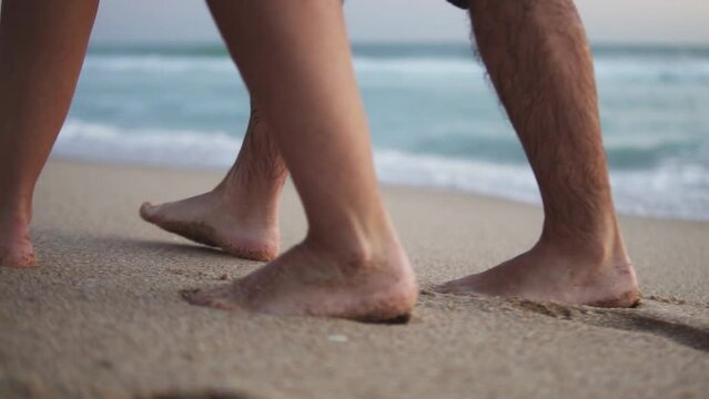 Slow motion handheld shot of a couple in love taking a romantic walk along a sandy beach with calm waves in the sea 