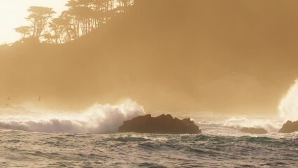Epic slow motion shot on RED camera of powerful wave crashing with white splashes at rocky ocean cost in scenic golden sunset light and breeze wind. Copy background with energy of ocean water at coast